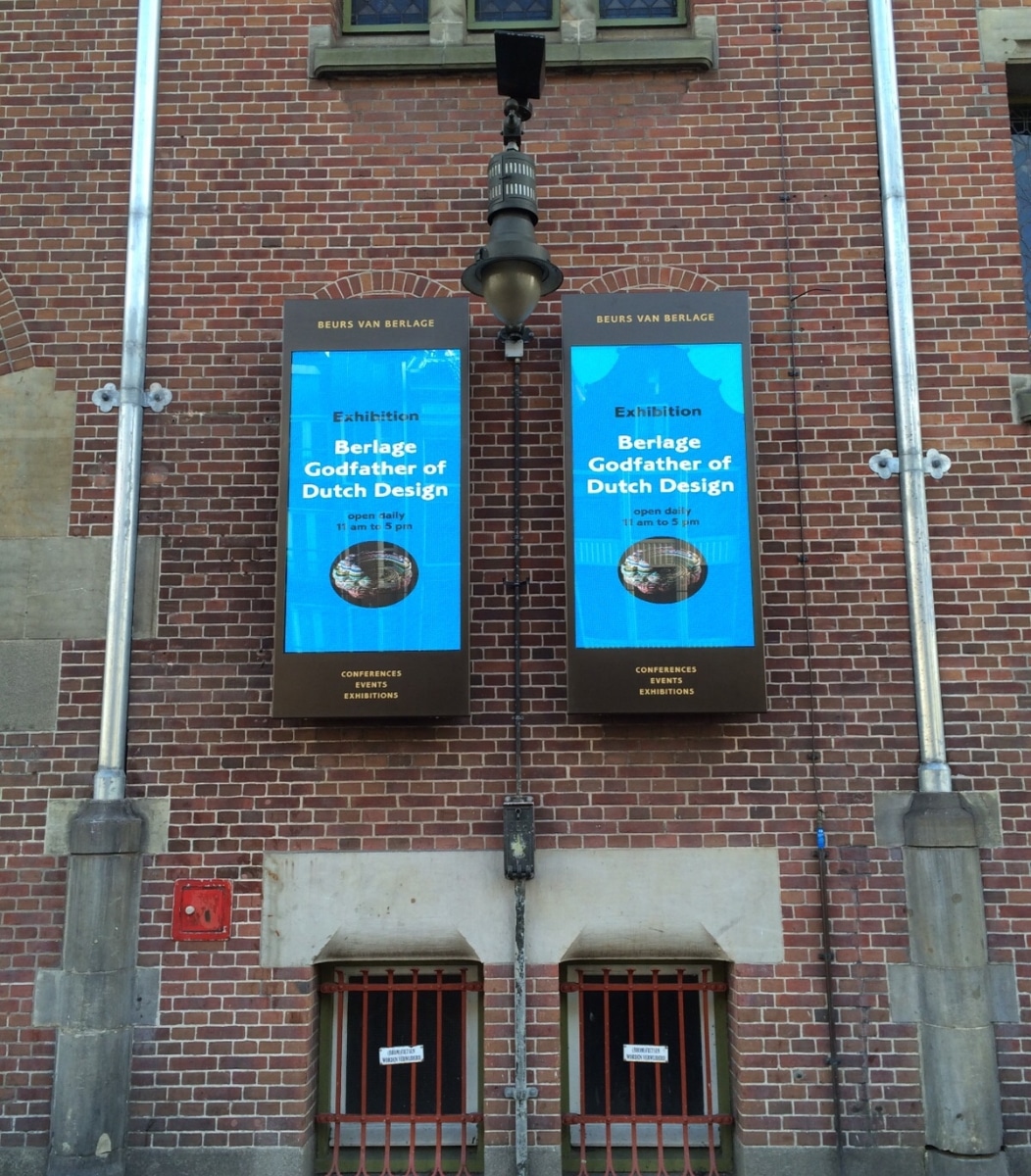 LCD schermen gemonteerd middels wandmontage tegen de muur van het pand van Beurs van Berlage.