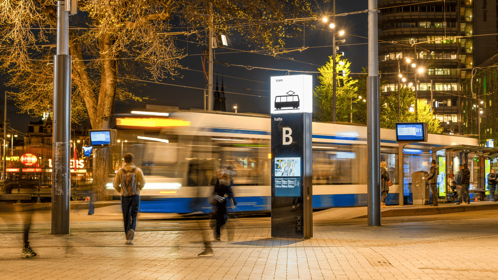 Een dynamische nachtopname van een Vidiled wayfinding-zuil, geplaatst bij een tramhalte op Amsterdam Centraal Station, voor real-time reisinformatie.