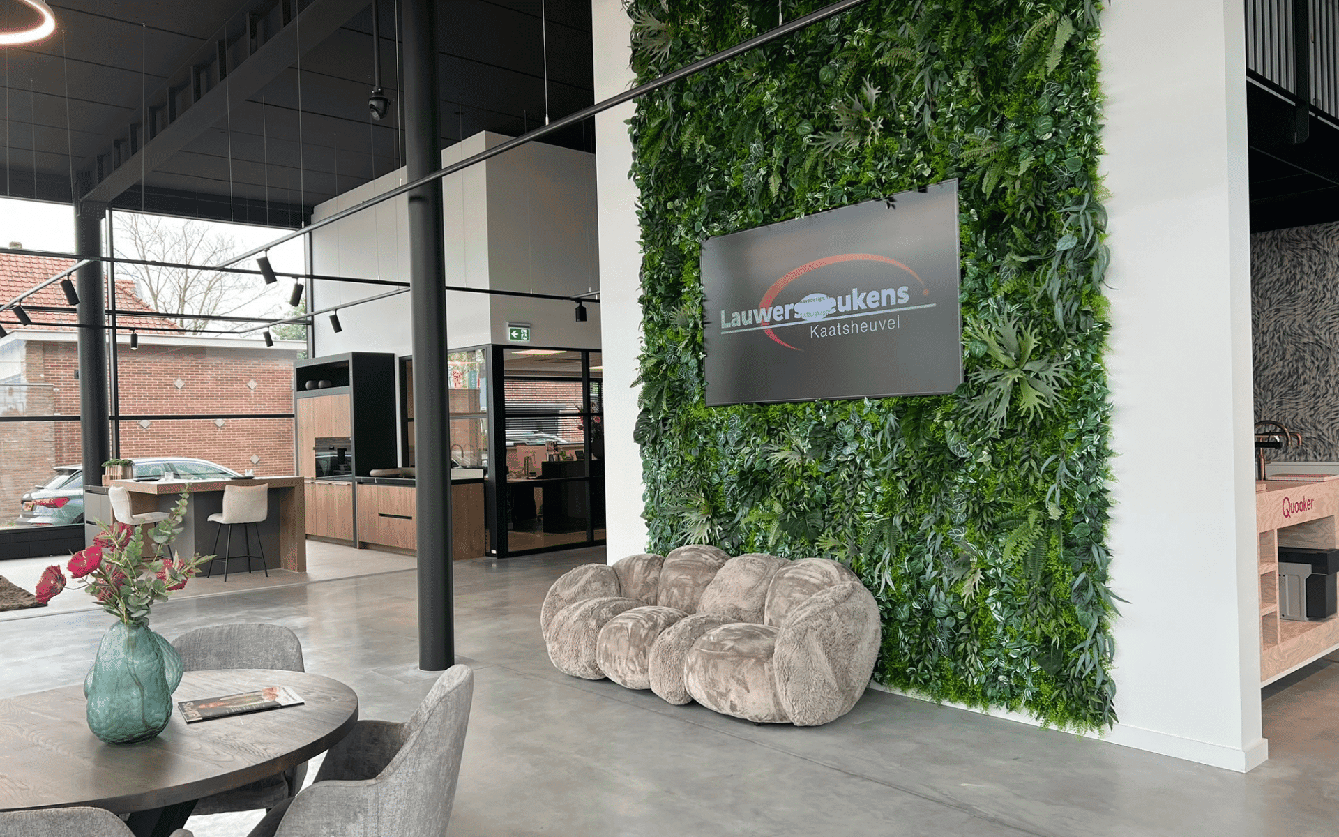 Vidiled LCD-scherm gemonteerd aan witte wand in keukenwinkel, toont productafbeelding in moderne showroomopstelling