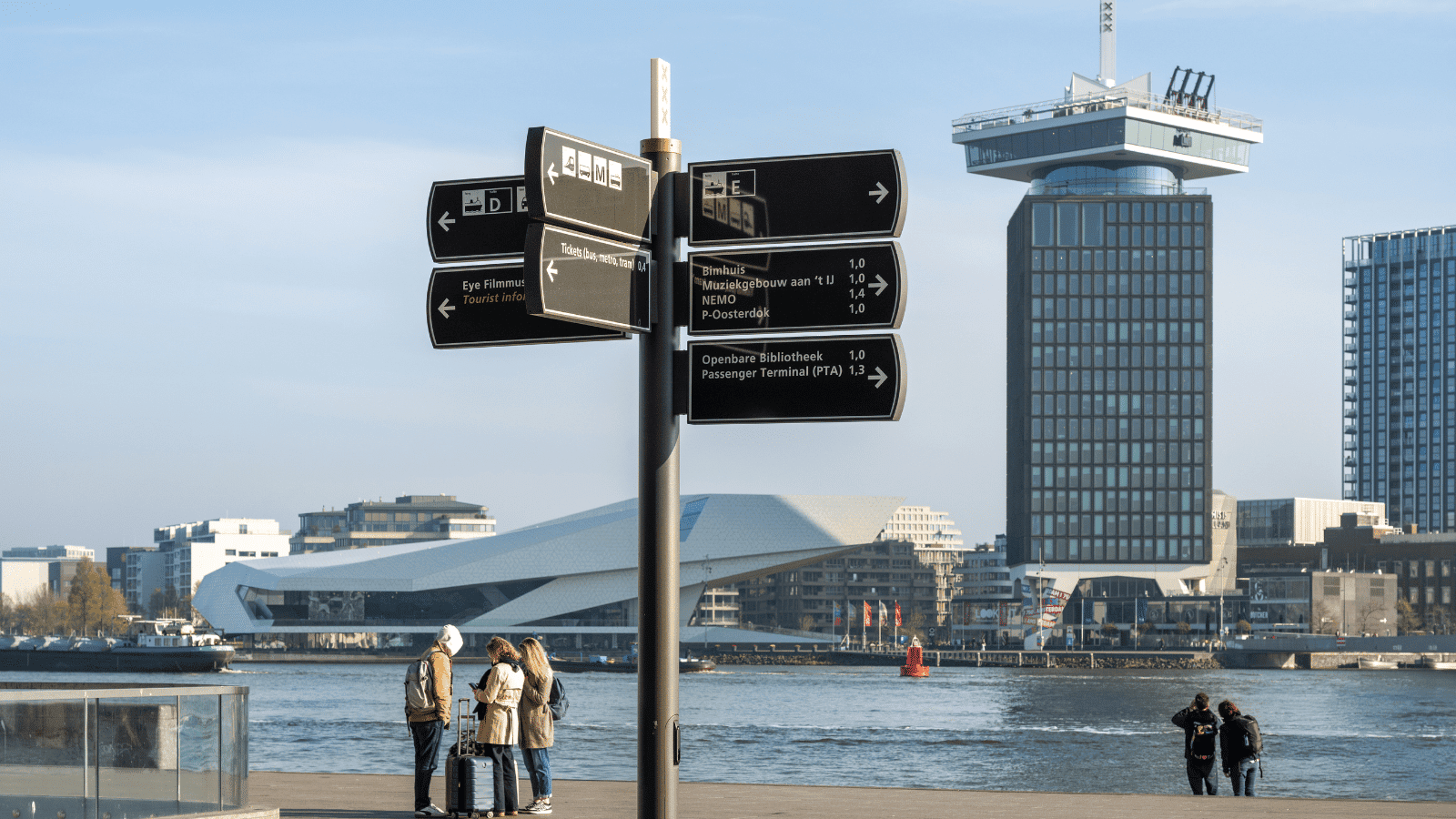 Overdag overzicht van de robuuste, multi-directionele wayfinding-borden van Vidiled, die reizigers wegwijs maken langs de kade bij Amsterdam CS.