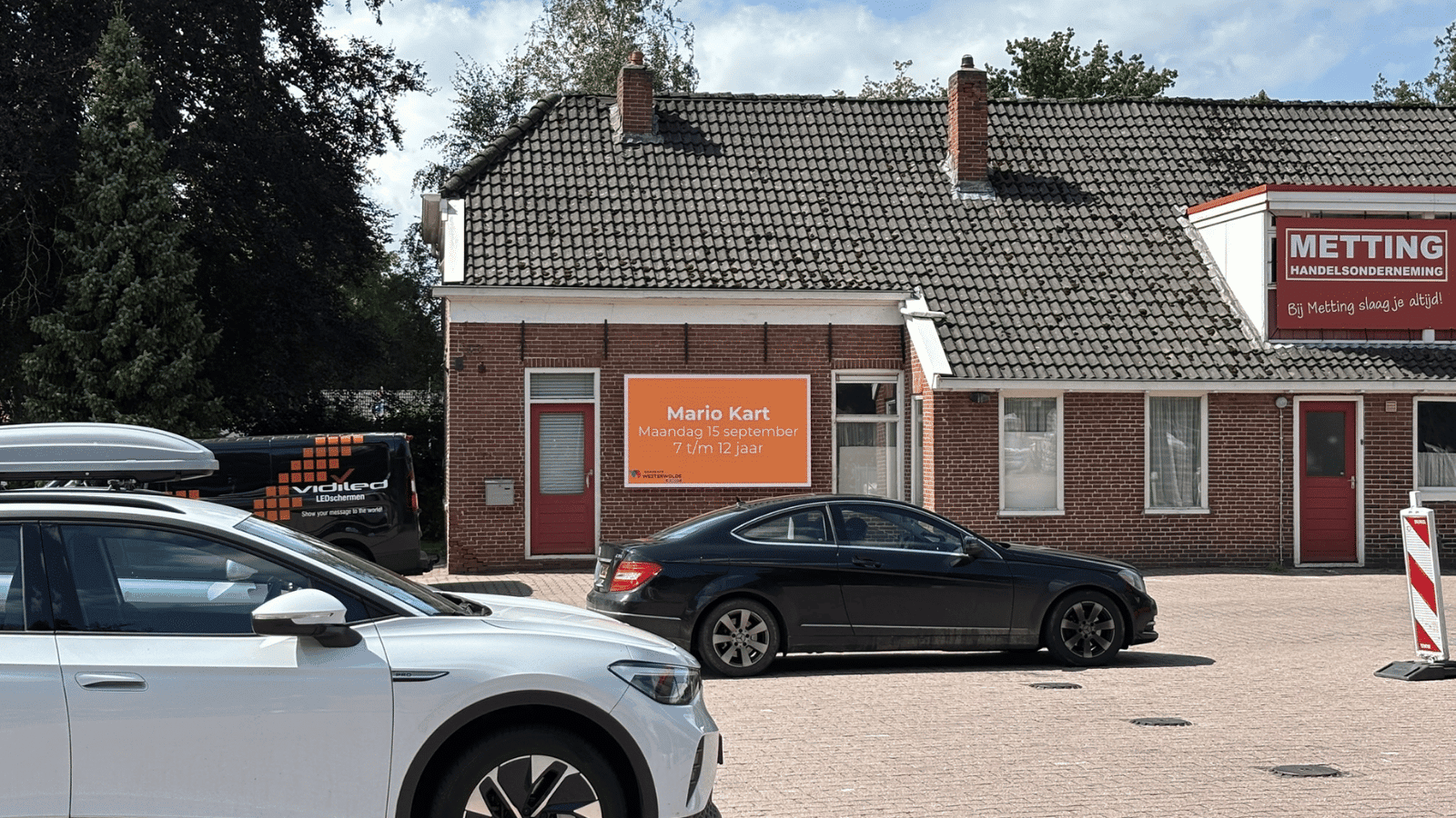 Buitenopstelling van een Vidiled LED-scherm aan een bakstenen muur in Bellingwolde, tonend een oranje informatiebord voor sportactiviteiten